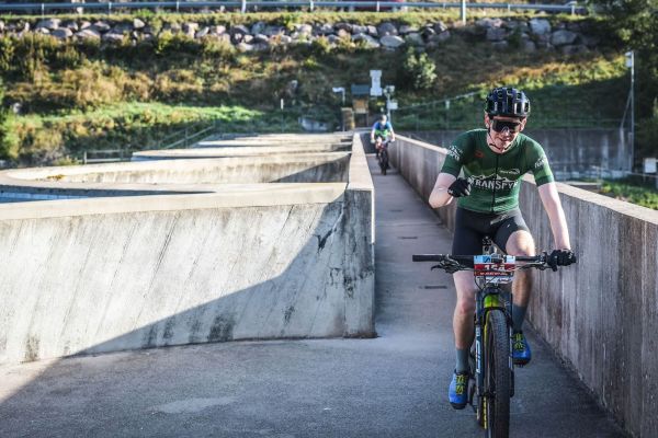 Mountainbiker fährt über einen Beton-Damm, ein weiterer folgt im Hintergrund.
