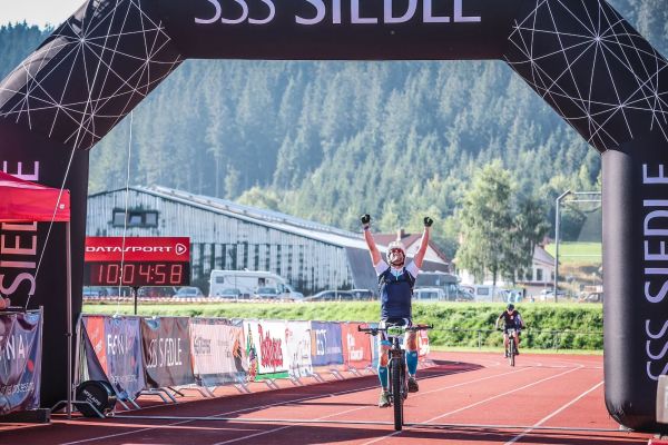 Mountainbiker fährt mit erhobenen Armen durchs Ziel im Stadion beim Schwarzwald Bike Marathon 2023