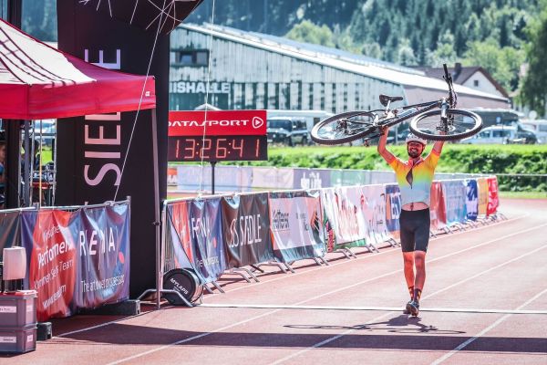Finisher überquert die Ziellinie im Stadion und hält sein Mountainbike jubelnd über dem Kopf
