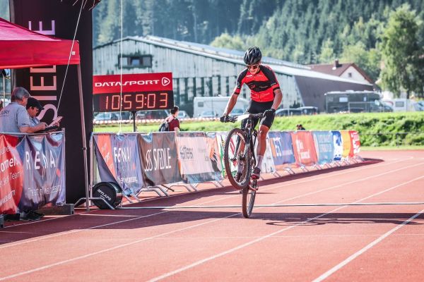 Mountainbiker zieht kurz vor der Ziellinie im Stadion einen Wheelie beim Schwarzwald Bike Marathon 2023