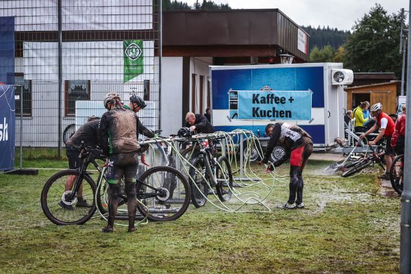 Teilnehmende reinigen ihre Mountainbikes an der Waschanlage, im Hintergrund „Kaffee + Kuchen“