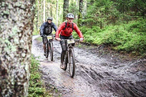 Zwei Mountainbiker fahren durch Schlamm und Pfützen auf einem Waldweg